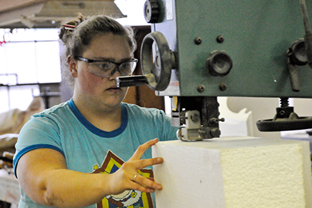 Scene shop apprentice Aimee Plant cutting styrofoam blanks for flowers